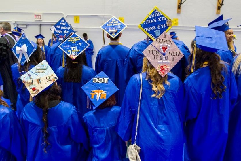 students in commencement regalia pose with the backs to camera, revealing a variety of messages on their hats